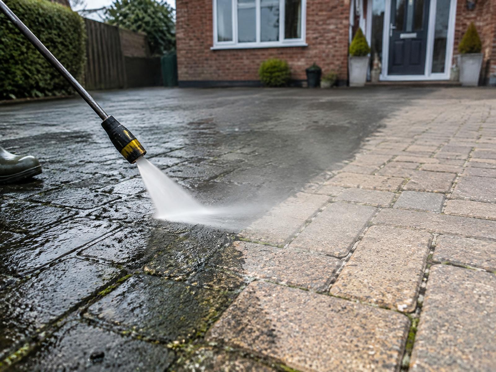 Pressure washer stripping dirt from a block-paved driveway, showing a sharp clean line